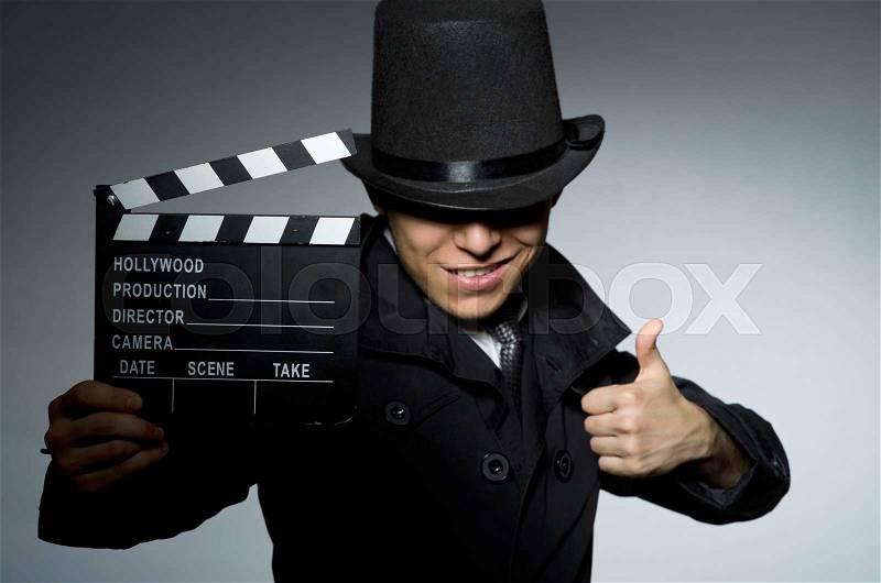 Young man with weapon and clapboard against gray, stock photo