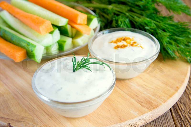 Fresh Greek Tzatziki yogurt dip (sauce) and assorted vegetables on wooden table, stock photo