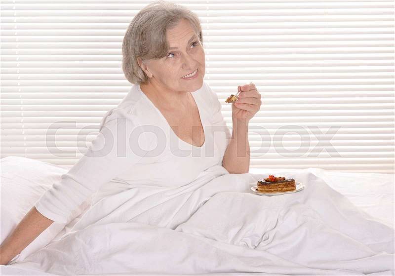 Beautiful older woman resting in the bedroom with cake, stock photo