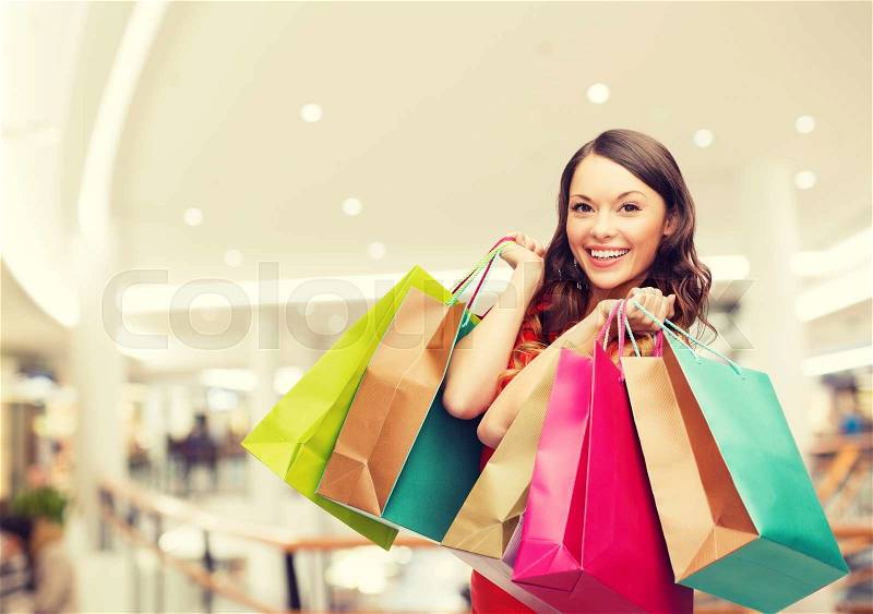 Happiness, consumerism, sale and people concept - smiling young woman with shopping bags over mall background, stock photo