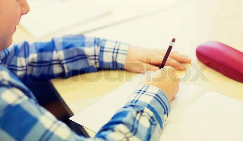 Education, elementary school, learning and people concept - close up of little schoolboy with notebook and pencil writing test at school, stock photo