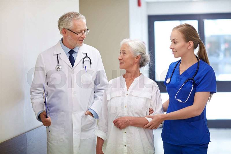 Medicine, age, health care and people concept - male doctor with clipboard, young nurse and senior woman patient talking at hospital corridor, stock photo