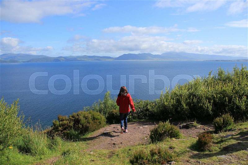 The girl makes a jump in the future and has a wonderful view over Dingle Bay in the county Kerry in Ireland in the summer, stock photo