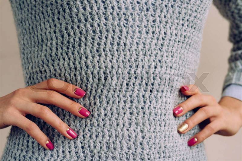Woman in a gray knitted sweater put her hands on her waist. On nails pink and golden manicure, stock photo
