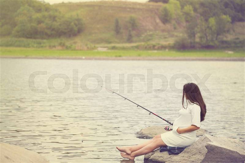 Young beautiful pregnant woman fishing on the river bank, stock photo