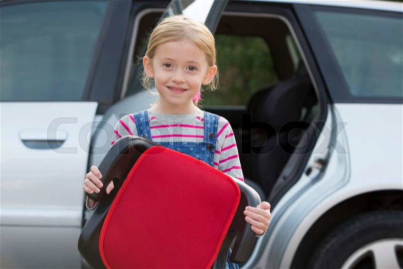 Portrait Of Girl Holding Booster Seat Standing Next To Car, stock photo