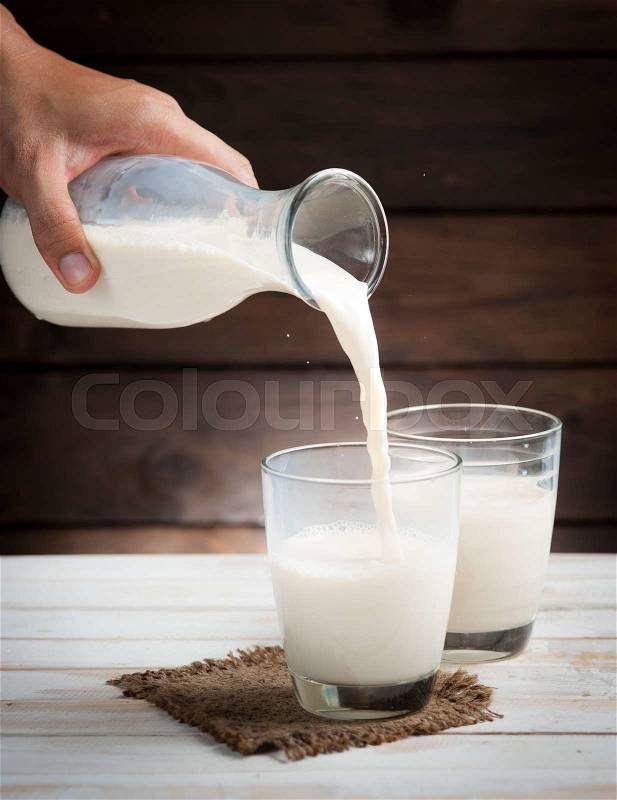 Milk from a jug pouring into glass on wooden, stock photo