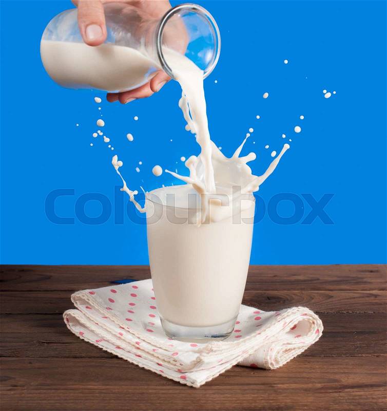 Milk from a jug pouring into glass on a blue background, stock photo