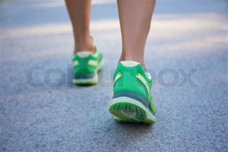Close up of female legs in sporty shoes running on asphalt road, stock photo