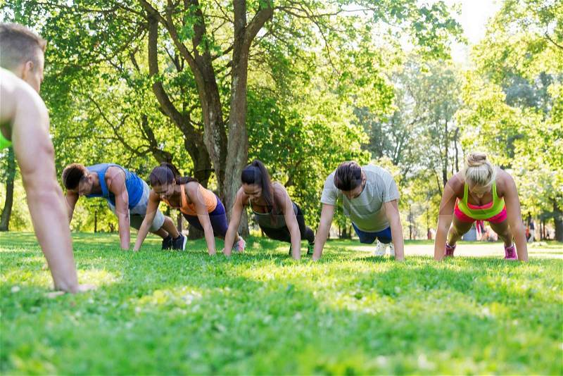 Fitness, sport, friendship and healthy lifestyle concept - group of happy teenage friends or sportsmen exercising and doing push-ups at boot camp, stock photo