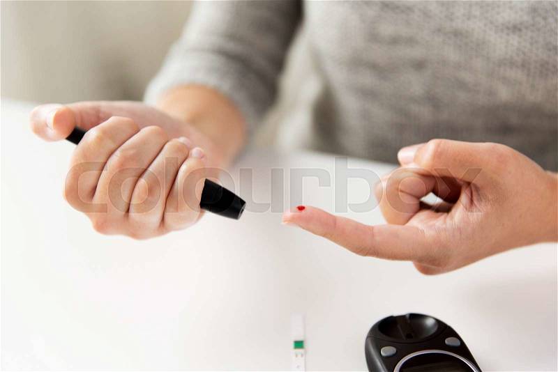Medicine, diabetes, glycemia, health care and people concept - close up of woman checking blood sugar level by glucometer at home, stock photo