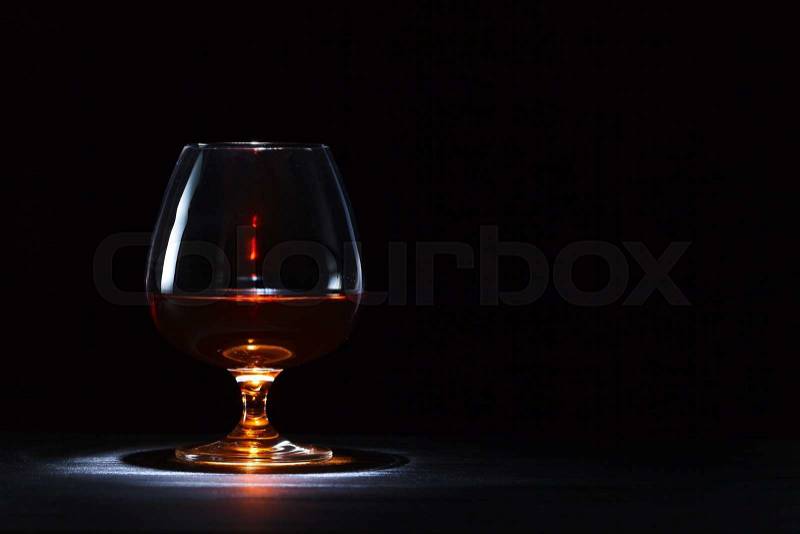 Snifter with brandy on black wooden table, stock photo