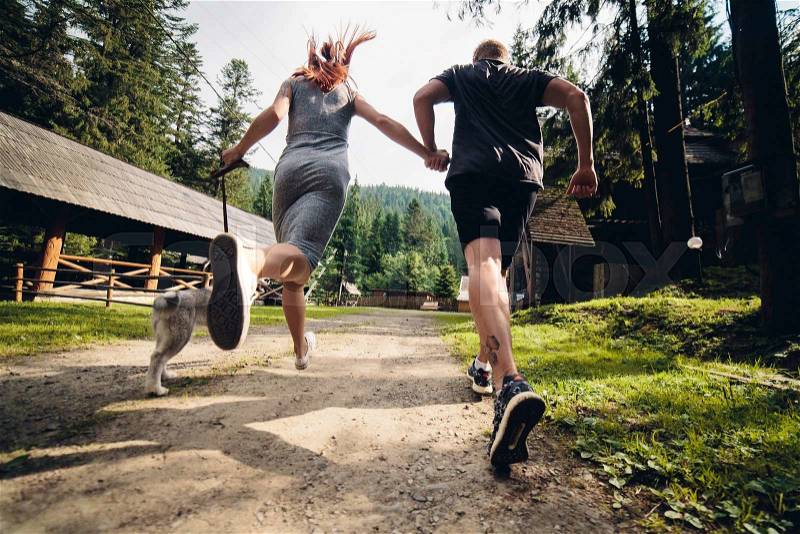Couple runs on road in the nature with dog to a house, stock photo