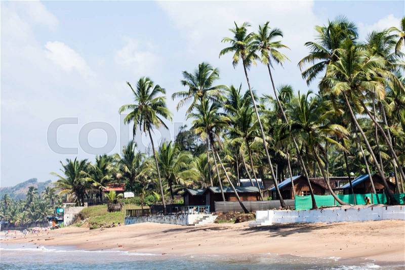 Exiting Anjuna beach panorama on low tide with white wet sand and green coconut palms, Goa, India , stock photo