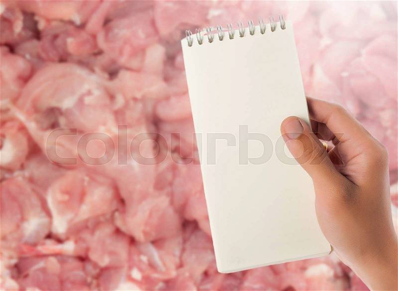 Hand hold blank notepad with space for text,raw pig meat as blur background, stock photo