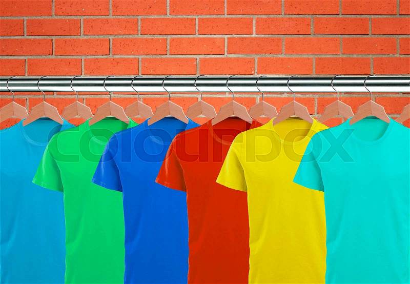 Lots of T-shirts on hangers over orange brick wall, stock photo
