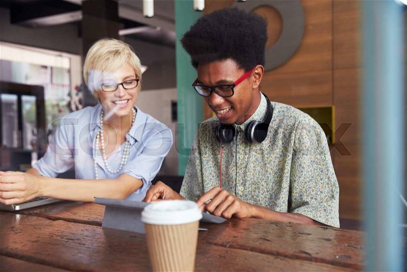 Two Young Businesspeople Working On Laptop In Coffee Shop, stock photo