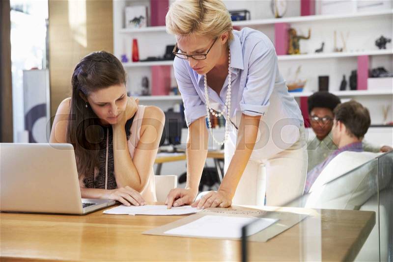 Two Businesswomen Working On Laptop In Busy Office, stock photo