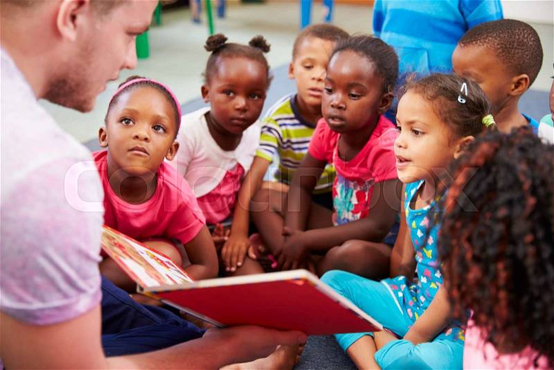 Volunteer teacher reading to a class of preschool kids, stock photo
