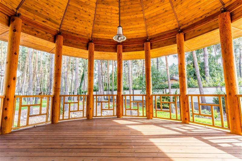 Large semi-circular porch in warm ecological wooden house with a garden view. On the ceiling hanging lamp. Porch is made of brown oak tree, stock photo