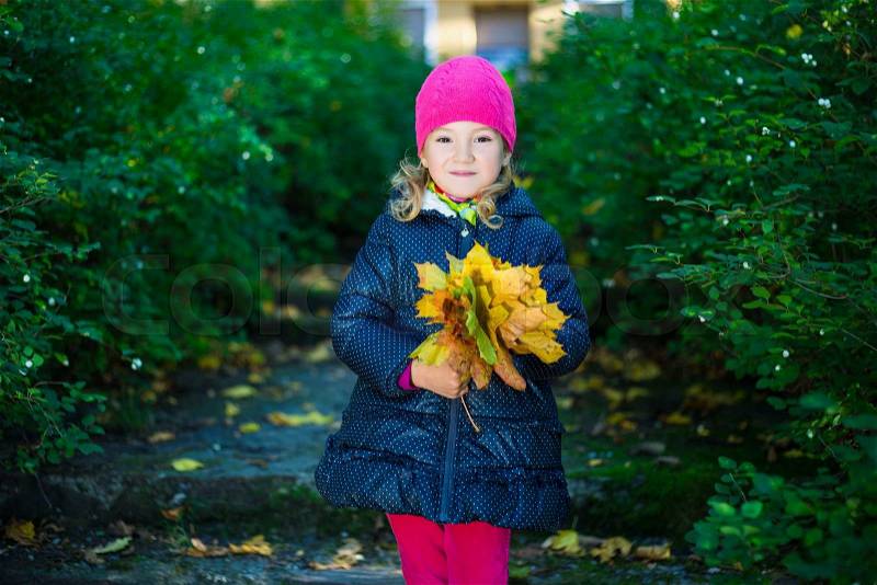 Happy little girl in warm clothes with yellow leaves posing in autumn park, stock photo