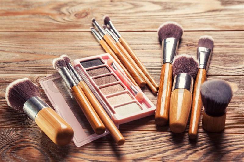 Brushes with cosmetics scattered chaotically on wooden background, stock photo
