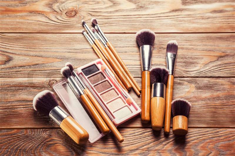 Brushes with cosmetics scattered chaotically on wooden background, stock photo