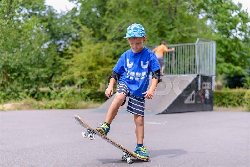 Happy boy practicing balancing on a skateboard with one end raised in the air as he enjoys the summer sunshine on vacation, stock photo