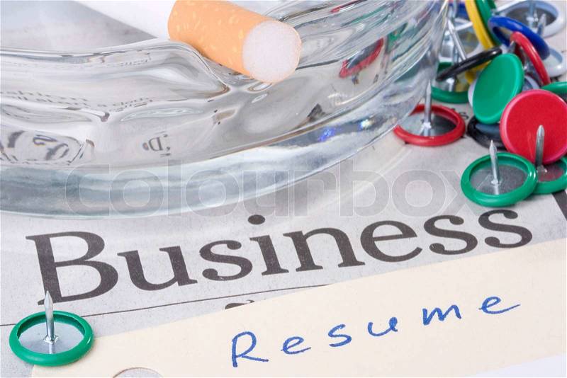 A manila resume folder laying on a business newspaper next to an ashtray with a filtered cigarette on it, stock photo