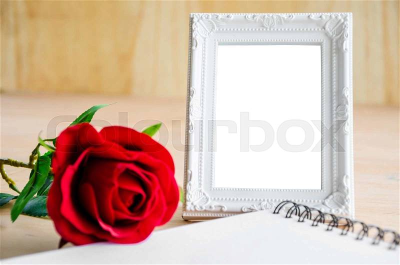 White vintage photo frame and red rose with open diary on wooden background. Save with clipping path, stock photo