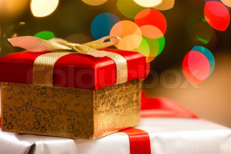 Red Christmas box with golden ribbon on background of colorful lights, stock photo
