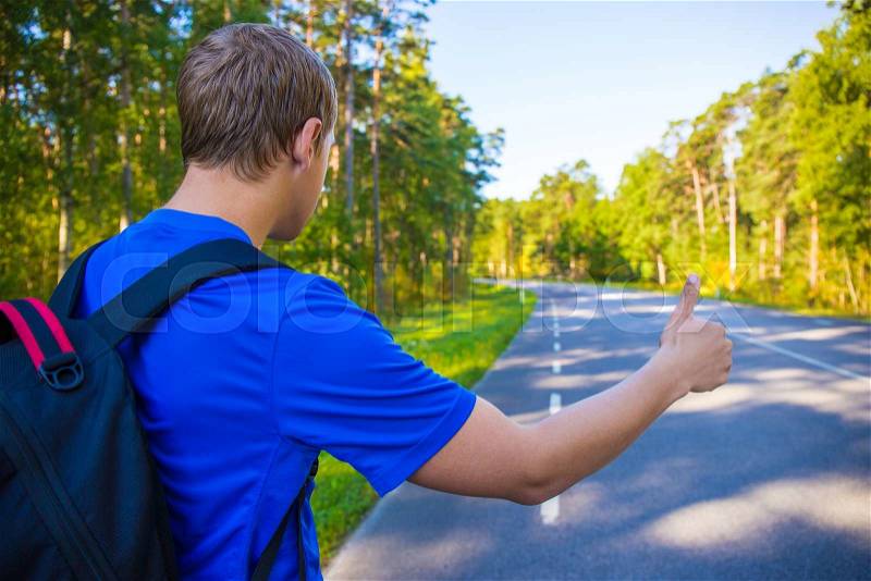 Hitchhiking concept - back view of man with backpack standing on forest road, stock photo
