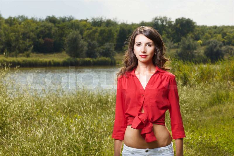 Beautiful young girl in red blouse on a background of green nature and lake in the summer, stock photo