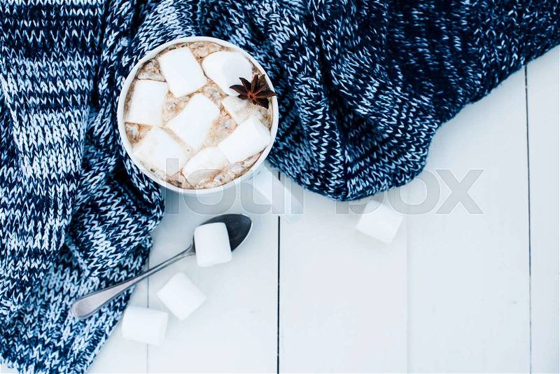 Cozy winter home background, cup of hot cocoa with marshmallow, old vintage books and warm knitted sweater on white painted wooden board background, stock photo