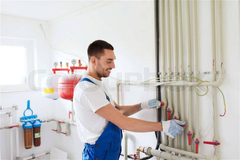 Building, profession and people concept - builder or plumber working with water pipes in boiler room, stock photo