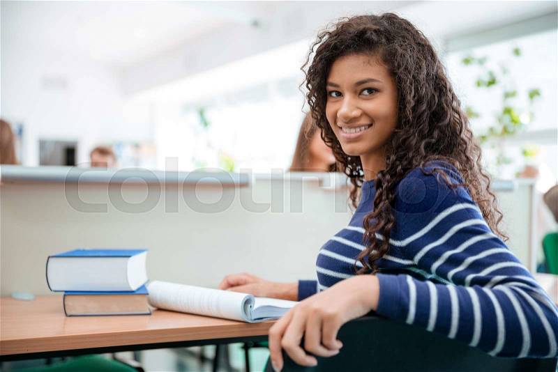 Portrait of a happy female student sitting at the desk in university and looking at camera, stock photo