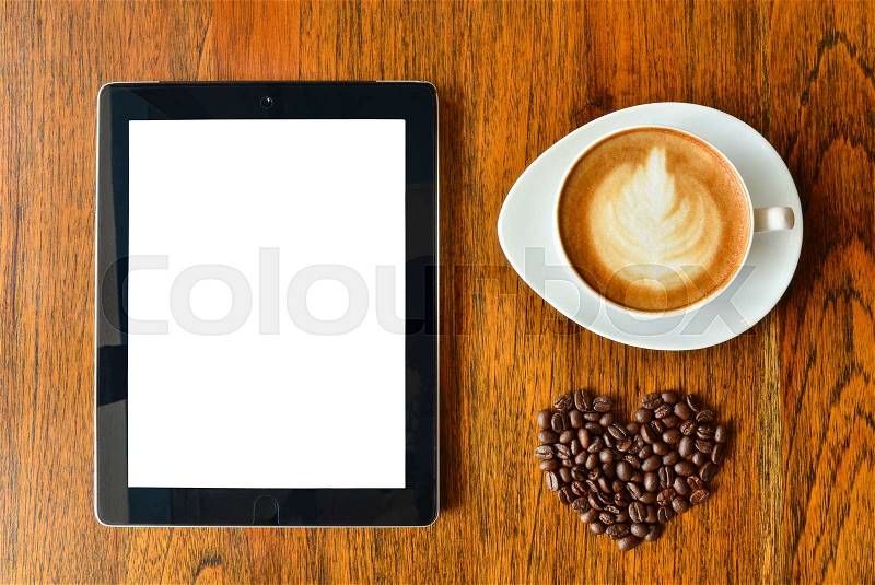 Digital tablet pc and a cup of coffee with heart shape on wood background, stock photo