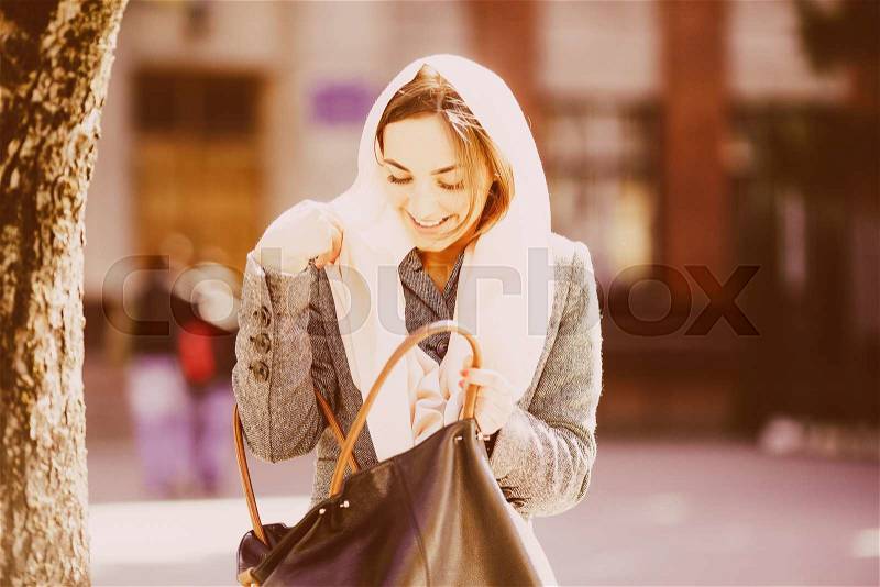 Beautiful girl on the street looking for something in a bag, stock photo