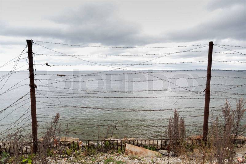 Imprisonment, restriction concept - barb wire fence over gray sky and sea, stock photo