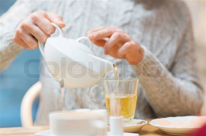 People, leisure and drinks concept - close up of man pouring tea from pot to cup at cafe, stock photo
