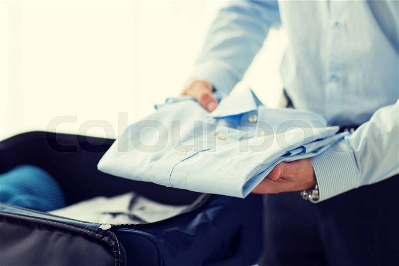 Business, trip, luggage and people concept - close up of businessman packing clothes into travel bag, stock photo
