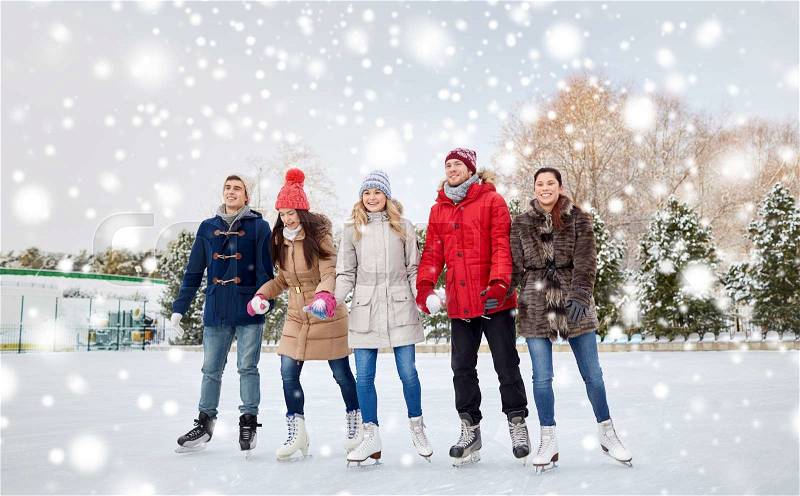 People, winter, friendship, sport and leisure concept - happy friends ice skating on rink outdoors, stock photo
