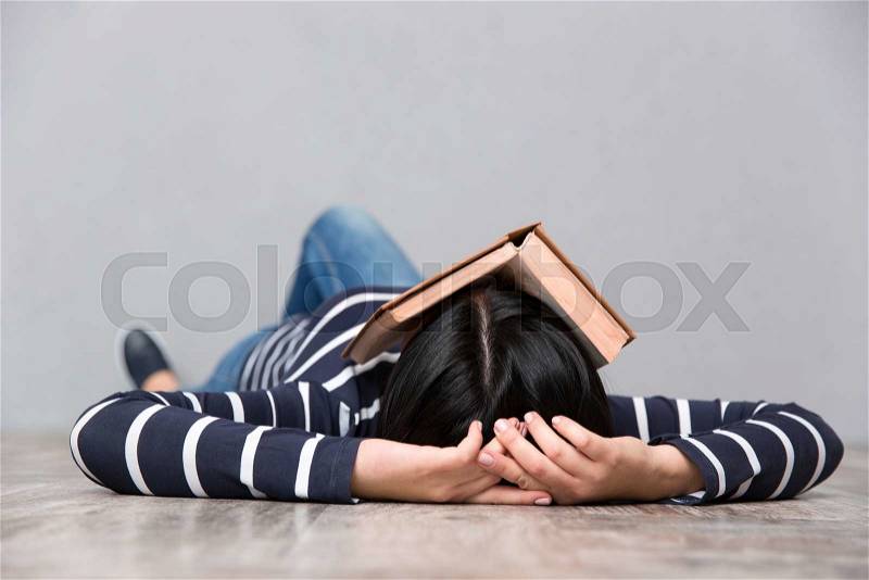 Young woman in striped jumper sleeping on the floor with book on her face, stock photo