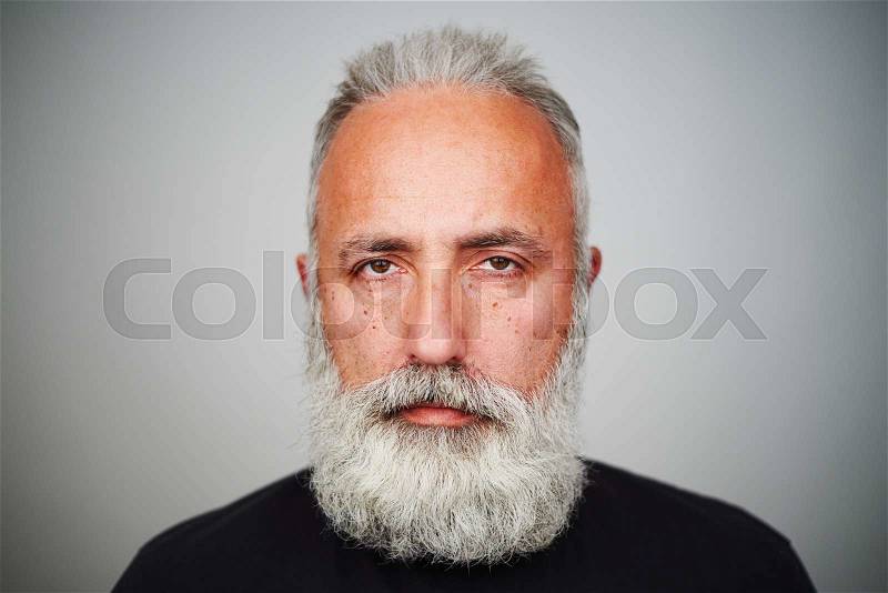 Close-up portrait of middle-aged man with grey-haired beard over grey background, stock photo