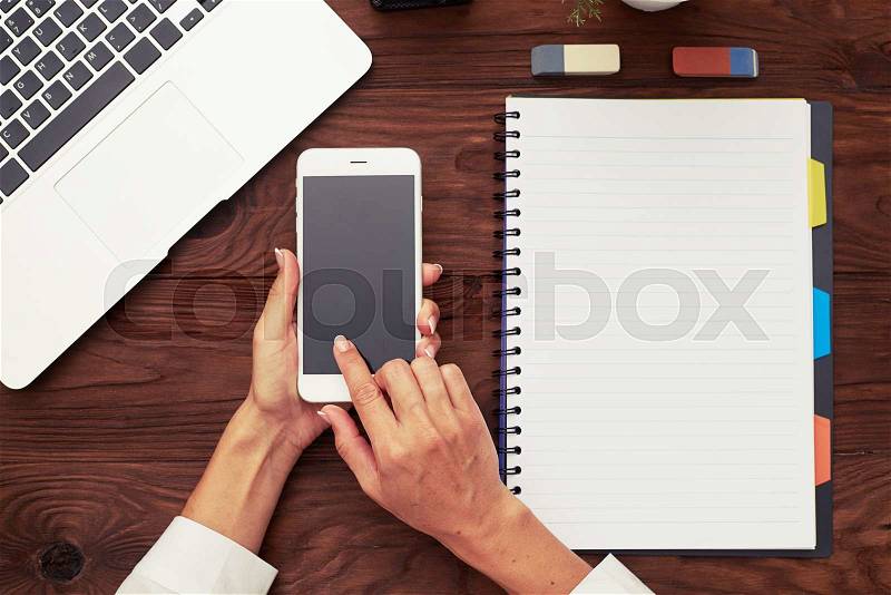 View from above on womans hands using smartphone over wooden table with business accessories, stock photo