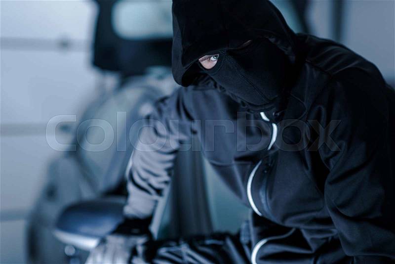 Car Theft Portrait. Successful Theft in Black Face Mask Seating on a Freshly Stolen Car, stock photo