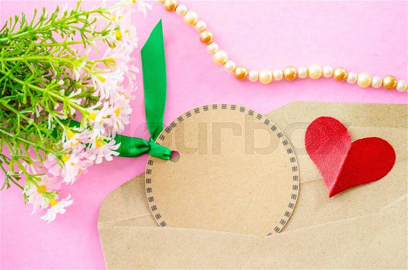 Blank brown paper tag and red heart paper with flower on pink background, stock photo