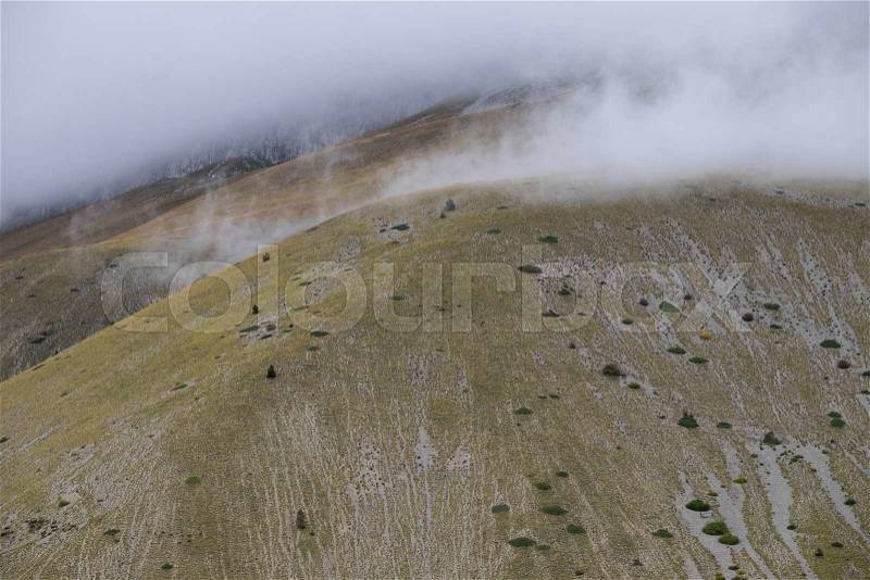Clouds between the green hills in the barren mountains of the Monti Sibillini in Umbria, Italy, stock photo