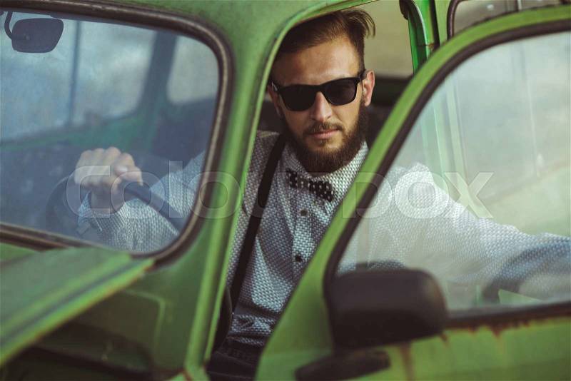 Portrait of a young stylish handsome man, wearing shirt and sunglasses, driving old car, stock photo