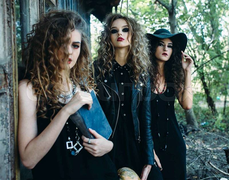 Three vintage women as witches, poses near an abandoned building on the eve of Halloween, stock photo